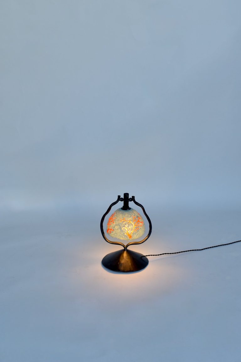 Peloria table lamp lit, black steel frame holding a recycled-plastic shade