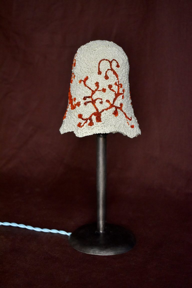 Small lamp with a white recycled-plastic shade patterned with red coral